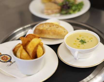 A tray with a bowl of soup, a bread roll and bowl of potato wedges. 