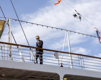 A man is standing by the railings on Britannia's Verandah Deck looking down onto the quayside. 