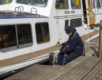 A maintenance man is securing protectors for the mooring ropes on Britannia's Royal Nore boat to prevent fraying. 