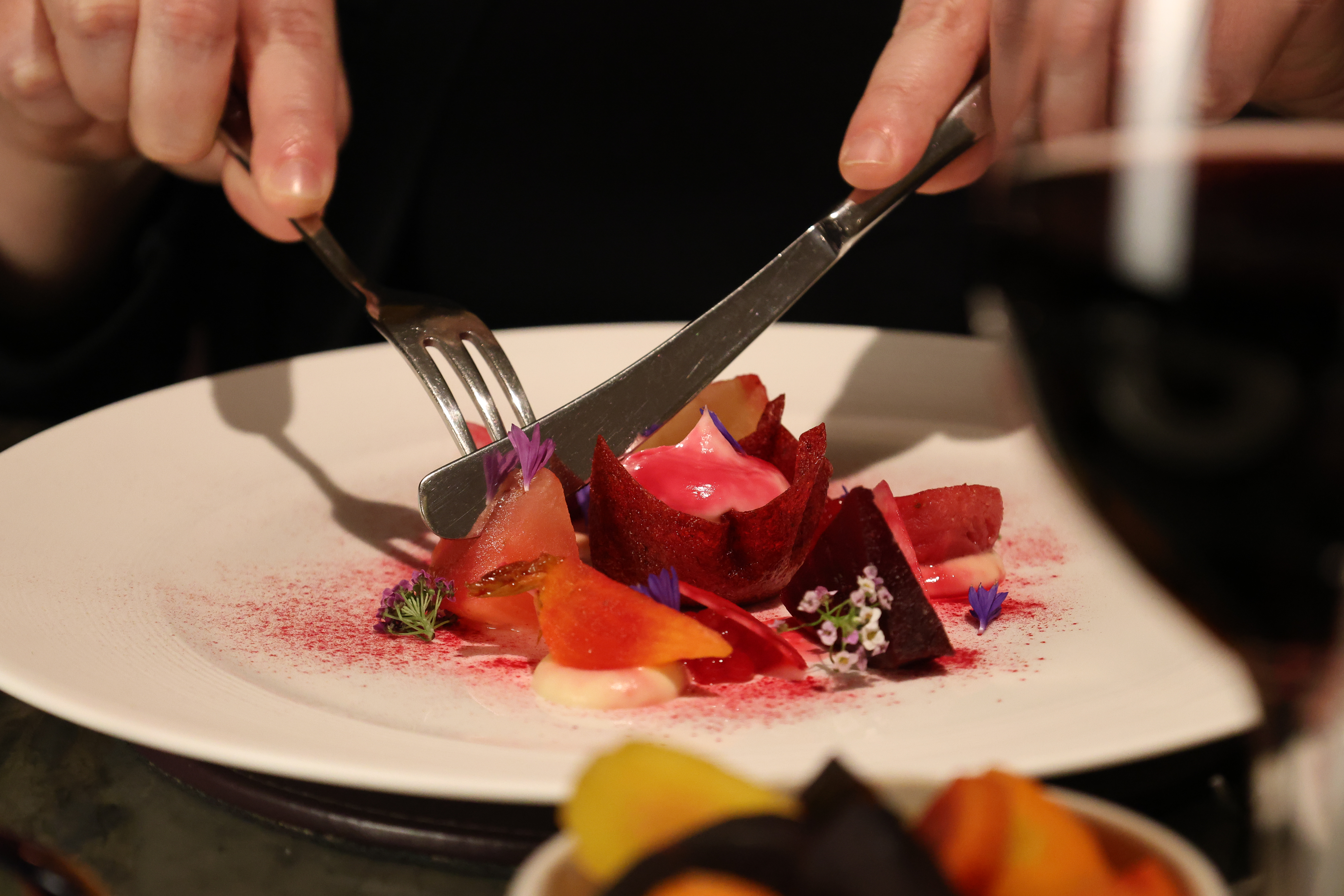 Hands are holding a knife and fork, cutting into a beetroot dish in the Lighthouse Restaurant aboard Fingal Hotel in Leith.