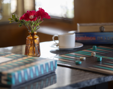A close up of a table with a board game on it. There is a vase with pink flowers and a tea cup and saucer. 