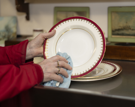 A close up of a hand holding a blue cloth polishing a china plate aboard Britannia in Edinburgh.