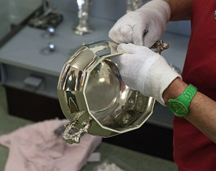 A silver bowl is polished by a Housekeeper wearing white cotton gloves.