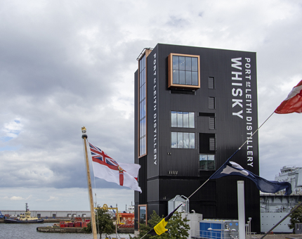 The new Port of Leith distillery black tall tower building with Britannia flagpoles in the foreground.