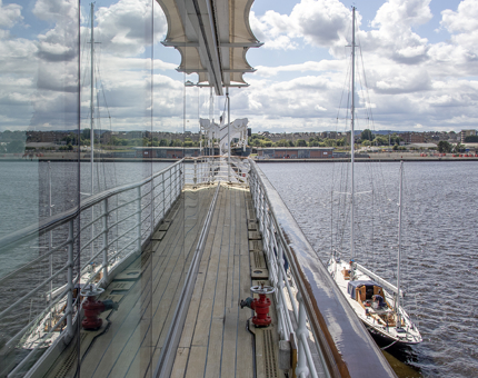 The tall windows outside the Royal Deck Tearoom reflecting the sky and water. There is a smaller yacht, Bloodhound beside Britannia.