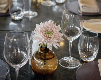 A dinner table in Fingal's Lighthouse Restaurant & Bar set with glasses and a pink flower in a vase.