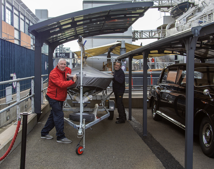 Two members of the Facilities Team wheel the sailing boat Coweslip underneath a new canopy cover on the Quayside.
