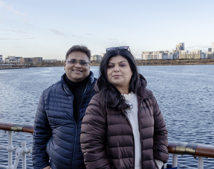 A man and a woman standing smiling with outside on deck with their backs to the water. 