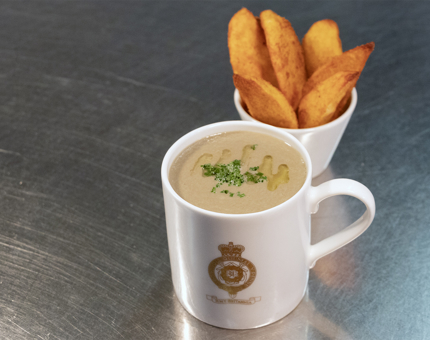 A Britannia crested mug of mushroom soup and bowl of potato wedges.