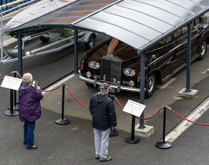 Two visitors looking at the classic Rolls-Royce car in the covered garage. 