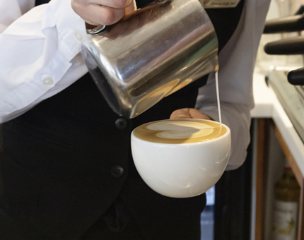 A coffee is being poured from a silver jug.