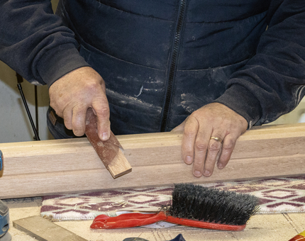 The man sanding the length of wood in the workshop. 