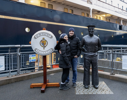 A couple pose next to a decorative perry buoy and statues of Yottie, Norrie.