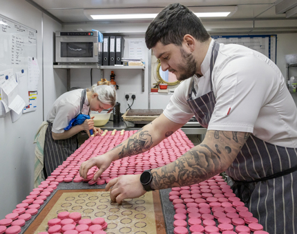 Two Pastry Chefs preparing bright pink macarons in the Galley.