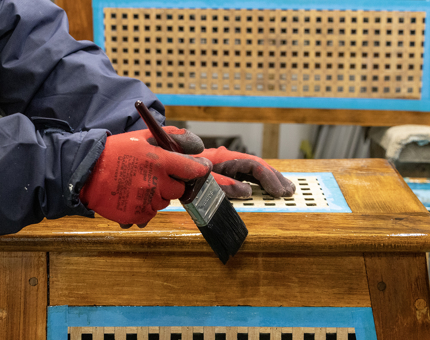 A close up view of a man varnishing a wooden rope box. 