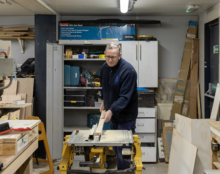 A member of the team cutting a piece of wood to create bases for the rope box seat pads. 