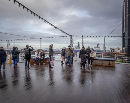 A number of visitors are listening to the audio guided tour on a wet day on the Verandah Deck at Britannia.
