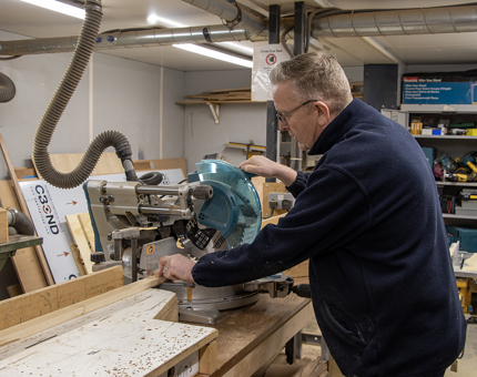 A man cutting wood for the 'A' frames in the workshop. 
