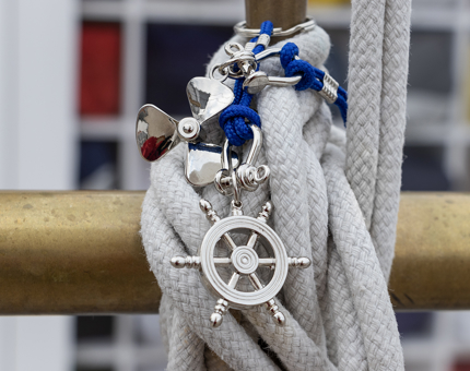 Silver coloured nautical inspired keyring of a ship's wheel and a propeller are arranged on a length of rope.