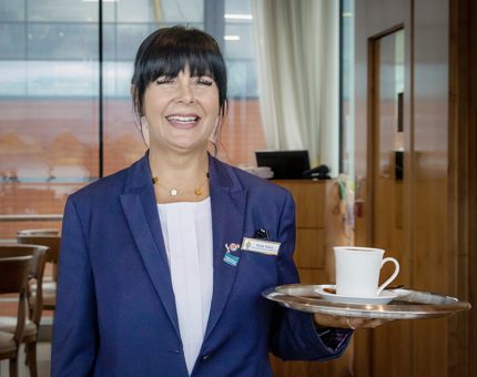 A member of the Tearoom team smiling and holding a tray containing a hot drink in the Tearoom.