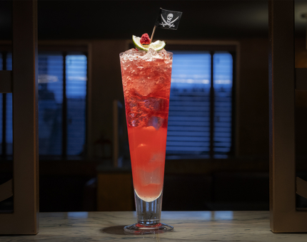 A red-coloured mocktail in a tall glass with a Jolly Roger flag on top. 