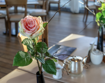 A pink rose in a vase on a table in the Royal Deck Tearoom.