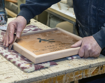 A team member from Maintenance sanding the wooden frame of a sign for Fingal. 