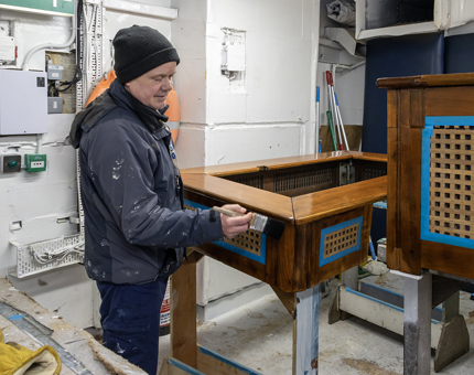 A man painting varnish onto a wooden hatch cover in the workshop. 