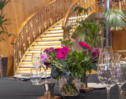 A bright pink floral arrangement on a dining table in Fingal's Ballroom. A curved staircase is in the background. 