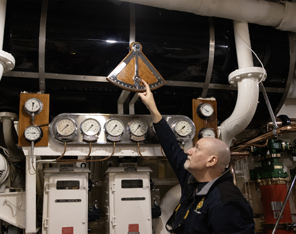 A Maintenance man looking up at the ship's clinometer, a triangular-shaped instrument.