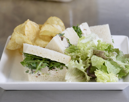 A chicken salad sandwich and crisps on a rectangular white plate.