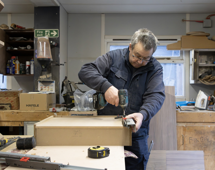 A Maintenance man using a drill and spirit level to build a wooden till point. 