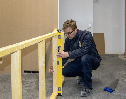 A Maintenance team member holding a spirit level next to a wooden frame. 