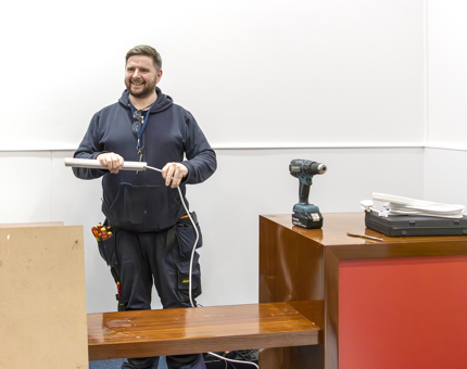 A team member from Maintenance installing extension leads behind the counter at the handset desk in the temporary Ticket Office. 