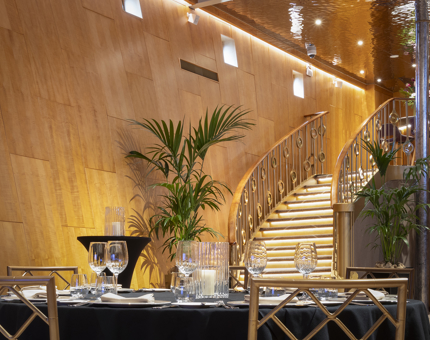 A table setting in Fingal's double-height Ballroom. A sweeping staircase and palm plants are in the background. 