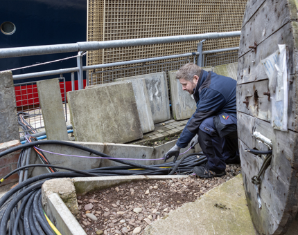 A man from Maintenance fitting large cables in the ground. 
