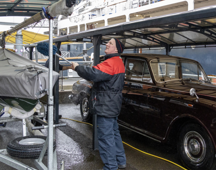 A man from Facilities using a long mop duster to clean inside the Garage where the vintage Rolls-Royce car is kept.