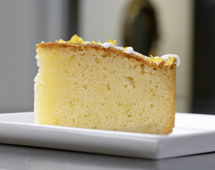 A large slice of lemon drizzle cake on a white plate. 