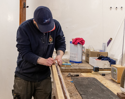A man in the workshop is sanding a handrail. 