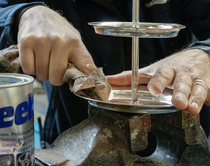 A member of the Maintenance Team polishing a silver-coloured cake stand. 
