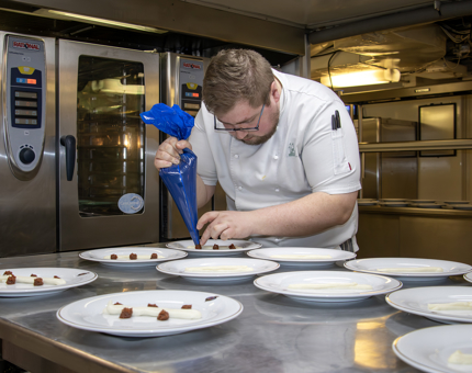 A Chef piping ingredients onto a row of plates in the Galley. 