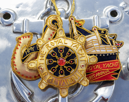 Three embroidered nautical novelty hanging decorations in gold and navy colours. One is a ship, one an anchor and one is a ship's wheel.