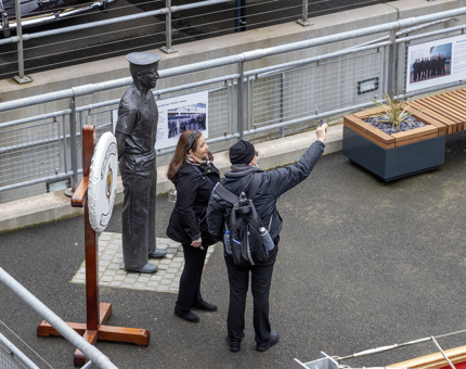 Two people take a mobile selfie next to the statue of Norrie, Britannia's longest serving crew member.