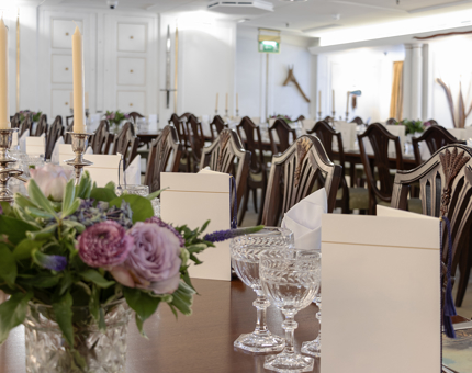 Inside the State Dining Room, which is set up for an evening event with long tables, menus, glasses and vases of pink flowers. 