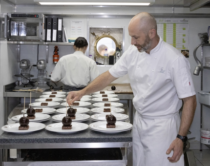 Two Chefs working in the Galley at Britannia. They are preparing exquisite chocolate desserts on plates.