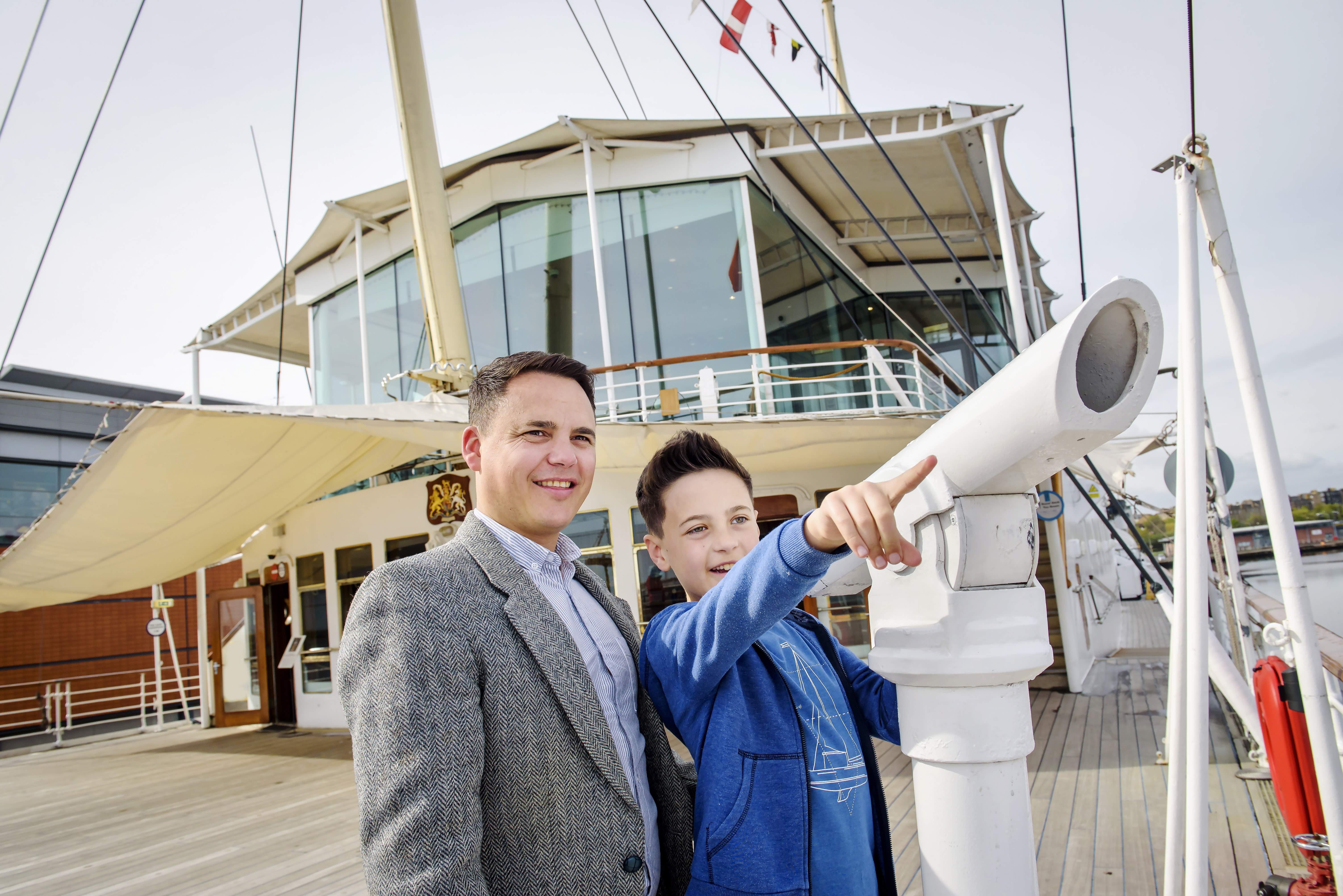 A man and boy on the Verandah Deck of The Royal Yacht Britannia in Leith. the boy is pointing into the distance.