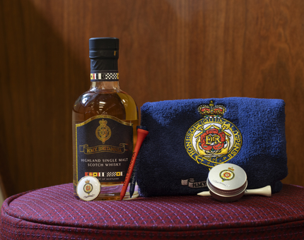 A bottle of Britannia whisky, a golf markers tin, golf tees, and a golfers towel. 