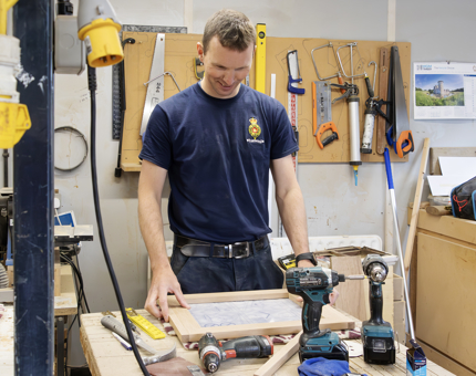 A Maintenance team member lays out a wooden frame on a worktop.