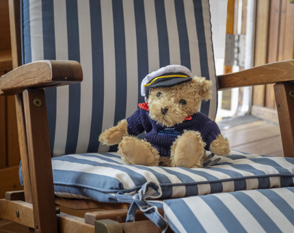 A cuddly teddy bear wearing a sailor's hat and sitting in a stripy chair.