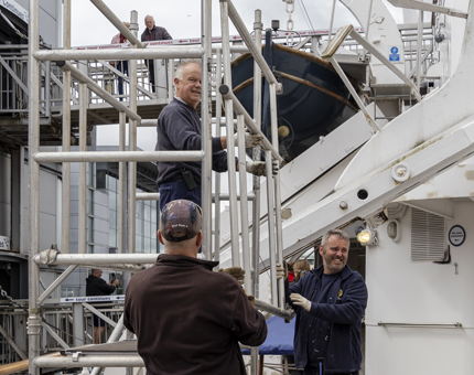 Three members of the Maintenance team are building scaffolding on the Port Shelter Deck.